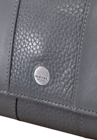 Prodotto in pelle grigia con una sezione superiore testurizzata e una parte inferiore liscia, accentuato da un logo in metallo e cuciture precise.