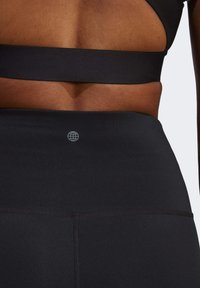 Sort aktivtøjsoverdel og matchende højtaljede leggings, der har en glat tekstur, tætsiddende pasform og en diskret logo på taljebåndet.