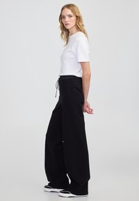 Biała bluzka z krótkim rękawem połączona z czarnymi, szerokimi spodniami o wysokim stanie. Spodnie mają elastyczny ściągacz w pasie i czarne akcenty na butach.