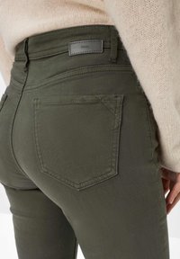 Olivgrüne High-Waist-Jeans mit enger Passform, ausgestattet mit einem Kunstleder-Label, zwei Gesäßtaschen und kontrastierenden Nähten.