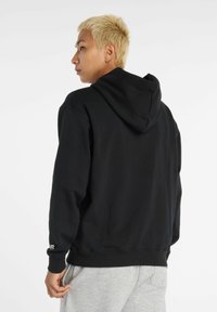 Sudadera negra de mezcla de algodón con un bolsillo canguro en la parte frontal, puños acanalados, hombros caídos y un detalle del logo en contraste en la manga.