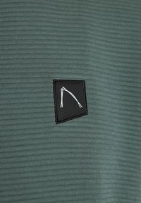 Donkergroene gestructureerde stof met een zwart vierkant patch en een witte lijnontwerp. De stof heeft een geribbelde uitstraling.
