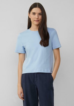 T-shirt bleu clair à manches courtes et col rond, fabriqué en coton doux. Il présente une coupe décontractée et une texture lisse, associé à un pantalon bleu marine.