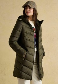 Olivovo zelená páperová bunda s chevronovým prešívaním, so zipsom vpredu a kapucňou. Obsahuje zipsové bočné vrecká a hladký, lesklý povrch.