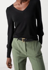 Maglione nero lavorato a maglia con scollo a V e maniche lunghe, abbinato a pantaloni verde chiaro e una cintura nera con fibbia dorata.