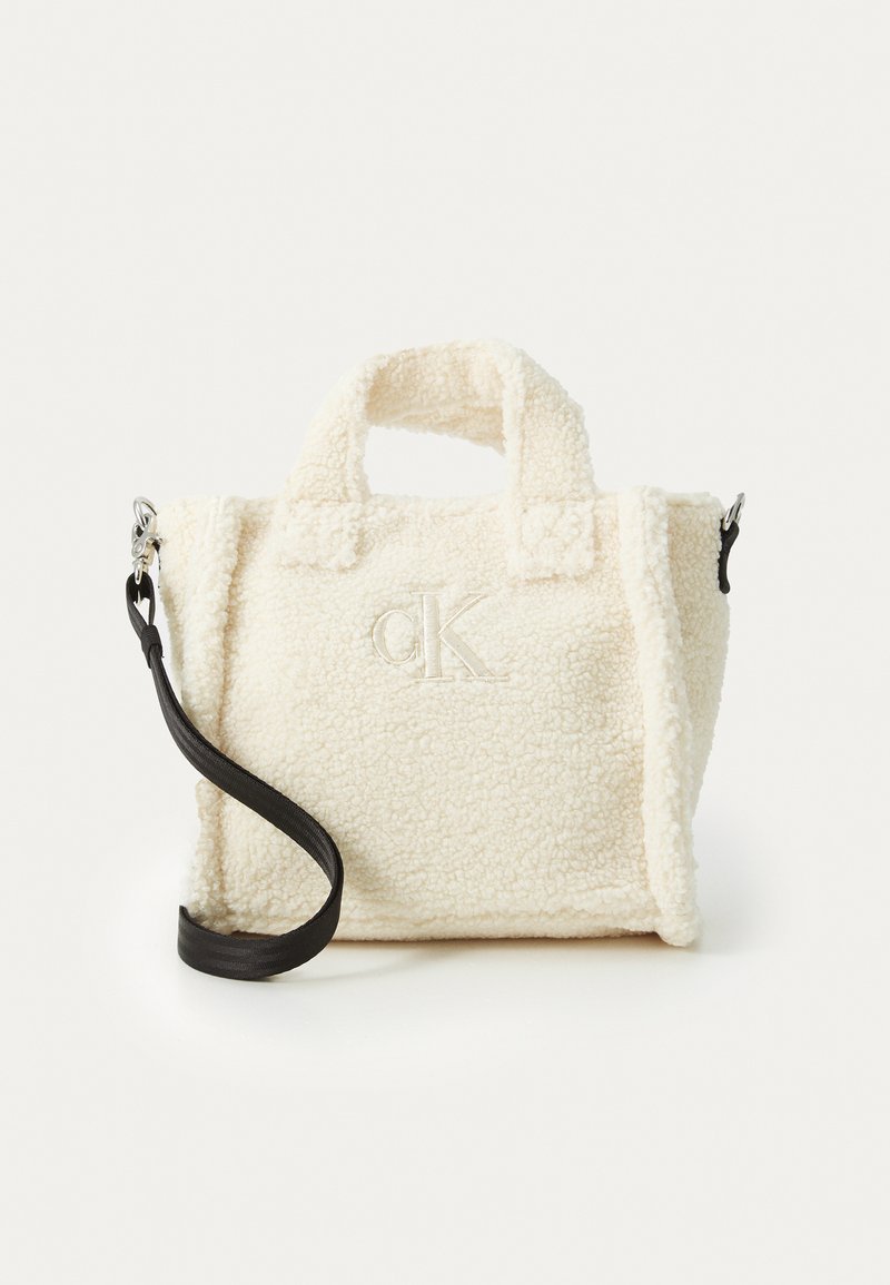 Kermainen teksturoitu laukku, joka on valmistettu fleece-materiaalista. Laukussa on kaksi lyhyttä kahvaa ja irrotettava musta olkahihna. Kirjailtu logoyksityiskohta.