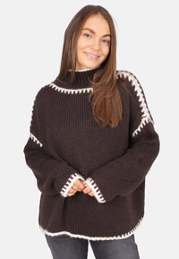 Brauner Strickpullover mit hohem Kragen, weißen gewellten Akzenten an den Bündchen und dem Saum sowie einer lockeren, übergroßen Passform.