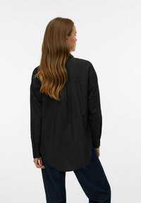 Maglietta nera a maniche lunghe con colletto, caratterizzata da decorazioni sulle maniche. Il design presenta un orlo arrotondato e una texture liscia.