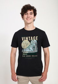 Černé tričko s grafickým designem vintage tenisky. Text zahrnuje "Vintage," "Launch Party" a "Old Skool Rules!" v kontrastních barvách.