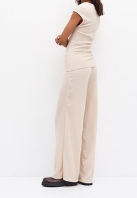 Haut beige clair en maille à manches courtes, associé à un pantalon beige à jambes larges. Le bas présente une texture côtelée, et les chaussures sont marron foncé avec une semelle épaisse.