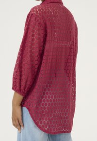 Burgundské krajkové tričko s kulatým výřezem, tříčtvrtečními rukávy a mírně zakřiveným spodním lemem. Měkká, průhledná textura.