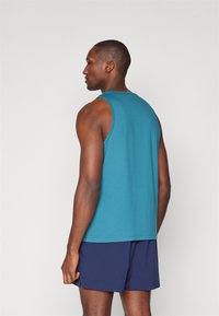 Herre uten ermer bomullstopp i teal, med rund hals og brede armer, kombinert med marineblå shorts. Enkelt, ensfarget design.