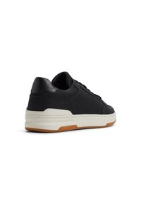 Zapatillas negras con una parte superior de cuero liso, mediopie blanca y suela de goma marrón. Presentan un diseño minimalista y detalles perforados en los lados.