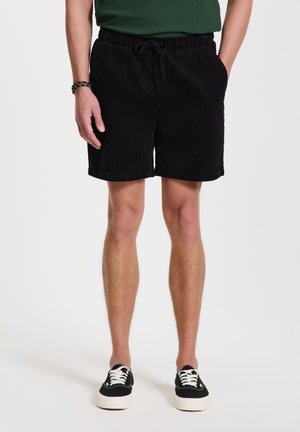 Black corduroy shorts with an elastic waistband and drawstring, featuring a textured surface and a straight hem. Worn with black shoes.