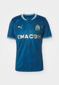 Maillot de football bleu foncé avec col et bordure de manches bleu clair, logo Puma doré, écusson du club de Marseille et texte sponsor "CMA CGM" en doré.