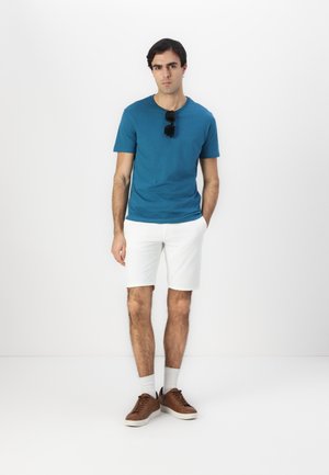 Teal short-sleeve t-shirt with a round neckline, paired with white shorts. Brown sneakers, white socks, and black sunglasses complete the look.
