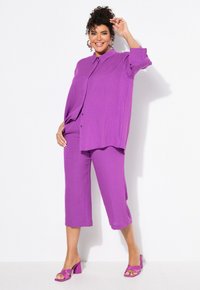 Conjunto de dos piezas en color púrpura que incluye una blusa holgada con botones, cuello y pantalones anchos cortos. Textura suave, combinado con sandalias de tacón cuadrado a juego.