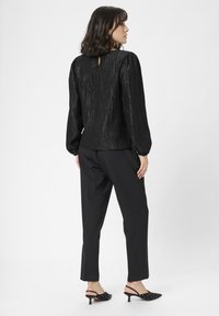 Bluză neagră cu textură, cu mâneci bufante și un accent în formă de cheie la spate, asortată cu pantaloni negri tailor-uiți și sandale cu vârf deschis și饰.