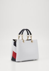 Struktureret håndtaske i hvid tekstureret læder med gyldent hardware, med sorte håndtag og en sideaccent med røde, marineblå og hvide striber.