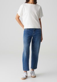 Hvid, struktureret kortærmet top parret med lyseblå lige ben jeans. Har hvide sneakers med beige såler og blå accenter.