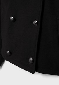 Cappotto nero in misto lana con design doppiopetto, bottoni neri decorativi e finitura strutturata. Include tasche laterali.