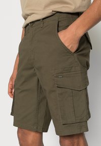 Pantaloni cargo verde oliva con tasche laterali, vestibilità normale e tessuto resistente. Presentano dettagli cuciti e chiusura con bottone.