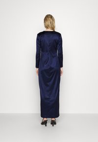 Long-sleeved navy satin dress with a fitted silhouette, smooth texture, and a subtle sheen, featuring a straight back and black high heels.