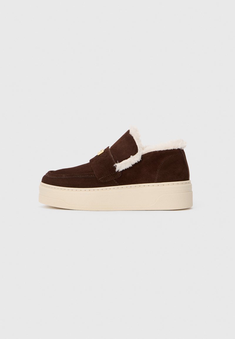 Mocasini din suede maro, cu căptușeală din blană albă și talpă groasă din cauciuc bej, fotografiat din lateral pe un fundal alb.