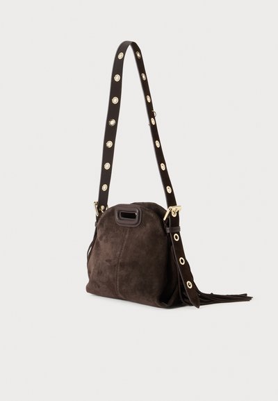 Sac à main en daim marron foncé avec une large sangle avec œillets dorés et ferrures dorées, posé sur un fond clair uni.