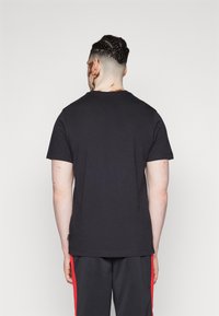 Musta puuvillainen t-paita, jossa on pyöreä kaula-aukko ja lyhyet hihat, päällä takaperin. Sileä pinta, yksinkertainen muotoilu, ilman näkyviä kuvioita.