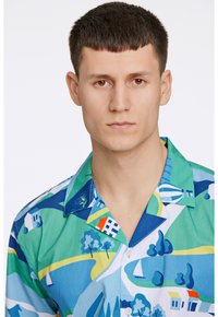 Camicia a maniche corte con bottoni, caratterizzata da una stampa paesaggistica colorata nei toni del blu, verde e bianco. I materiali sembrano essere tessili con una texture liscia.