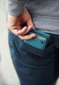 Blue fabric wallet partly visible in a dark pocket. The wallet features a simple design with a light gray accent and a discreet logo.