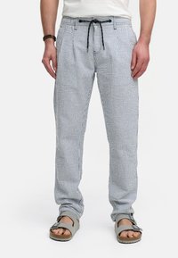 Stribede bukser i blå og hvid bomuldsstof med elastisk talje og snøre. Bæres med grå sandaler, hvilket fremhæver en afslappet pasform.
