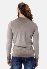 Camiseta de manga larga gris hecha de tela suave con un diseño ajustado. Ceñida en las muñecas, con una textura tonal sutil, combinada con jeans azules.