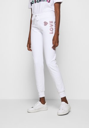 Modèle portant un pantalon de jogging blanc à cordon avec l’inscription LOVE en strass, un T-shirt assorti à motif graphique et des baskets blanches.