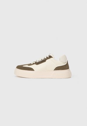 Low-top sneaker with beige sole, cream body, and olive green suede details, featuring white laces and a branded side label.