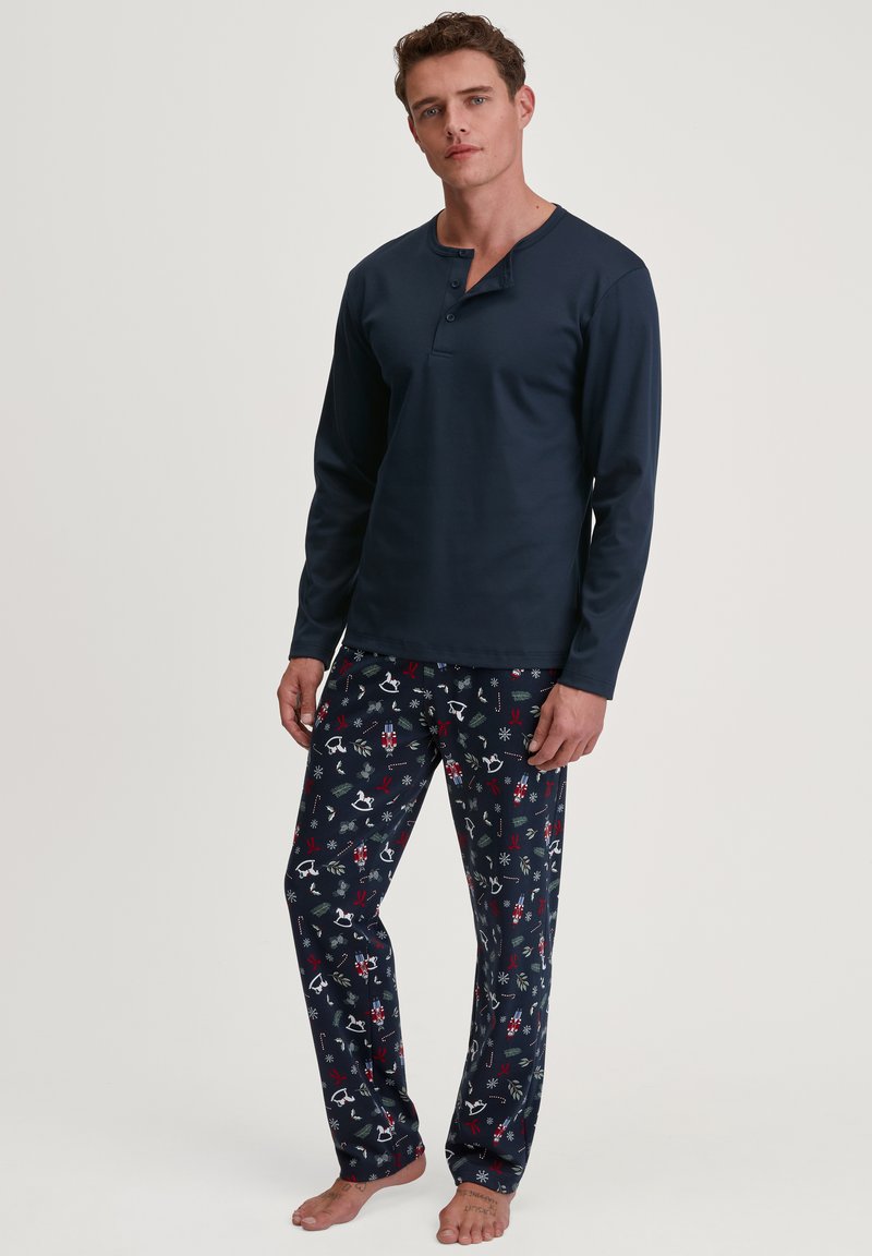 Marineblauwe lange mouwen pyjama shirt met een knoopsluiting, gecombineerd met pyjamabroek met een feestelijk patroon van sneeuwvlokken en feestdagen-thema iconen.