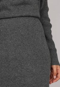 Pull en tricot côtelé gris avec des manches longues, un col montant et une silhouette ajustée. La texture semble douce et chaude.