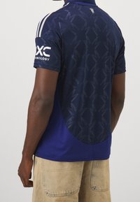 Granatowa koszulka sportowa z teksturowanym wzorem, krótki rękaw i logo na lewym rękawie. Wykonana z materiału odprowadzającego wilgoć.