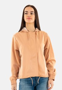 Coupe-vent léger de couleur pêche avec capuche, poignets élastiques et cordon de serrage réglable à l'ourlet. Matière lisse et brillante.