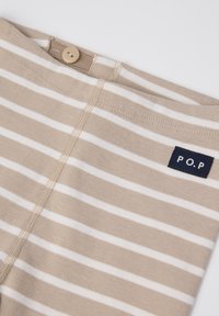 Beige katoenen mengsel kledingstuk met horizontale witte strepen, een knoopsluiting en een donkerblauwe label met "P.O.P" op de tailleband.
