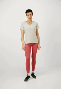 Tricou gri deschis cu mâneci scurte și decolteu în V, asortat cu colanți roz. Modelul poartă adidași negri cu talpă albă. Design simplu, mulat, în stil sportiv.