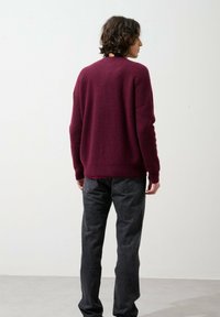 Maglione bordeaux a coste con maniche lunghe, vestibilità rilassata e scollatura rotonda. Abbinato a jeans grigio scuro, visto dal retro.