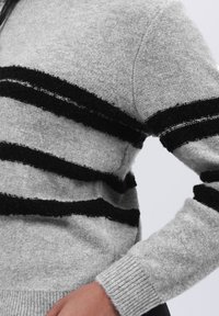 Grauer Pullover mit schwarzen, flauschigen Streifen, gerippten Bündchen und einer weichen Textur, gestaltet mit einem lockeren Schnitt und minimalistischen Stil.
