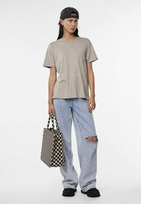 Gai brūnas kokvilnas T-krekls ar īsām piedurknēm, apvienots ar brīviem gaiši ziliem džinsiem ar plīsu pie ceļa, un melna un gaiši brūna pārnēsājamā soma ar rūtiņu rakstu.