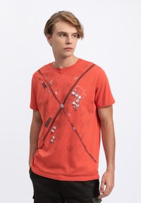 Rood katoenen t-shirt met abstracte grijze geometrische patronen en lijnen over de voorkant. Korte mouwen en ronde hals, casual snit.