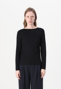 Svart langermet skjorte med rund hals; laget av glatt stoff; formsydd fasong; brukt med løse marineblå bukser.