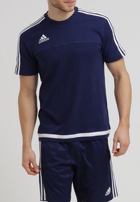 Granatowa sportowa koszulka z krótkimi rękawami, białe pasy na ramionach, faktura prążkowana na górze, logo na piersi. W zestawie z dopasowanymi szortami.