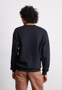 Felpa blu scuro con collo rotondo, polsini e orlo a coste. Realizzata in materiale morbido con una texture liscia. Design minimalista.