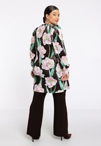 Langsleeve tuniek met een zwarte achtergrond en grote rozenmotieven in het roze, vergezeld van groene bladeren. Gedeeld met een paar donkerbruine flared broek.